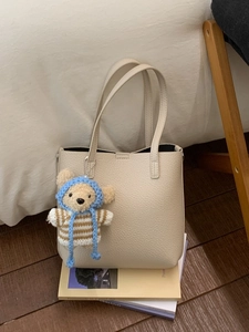 Chic cream pebble leather bucket bag with cute bear charm on books in a cozy setting