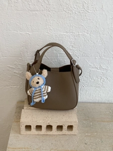 Minimalist tan lychee grain leather bucket bag with a cute bear charm on a textured wall