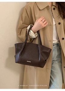 Détail du sac à main en cuir marron foncé avec plaque métallique sur une tenue élégante