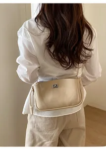 Detailansicht der beigen Baguette-Tasche mit Metalldrehverschluss und schmalem Schultergurt