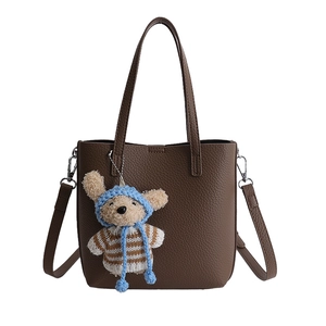 Détail d'un sac seau marron foncé texture litchi avec charmant pendentif ours bleu