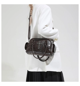 Détail du sac gothique marron foncé avec croix métallique et chaînes sur un blazer blanc