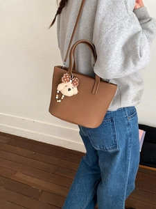 Brown PU leather bucket bag with teddy dog charm shown in a lifestyle model shot