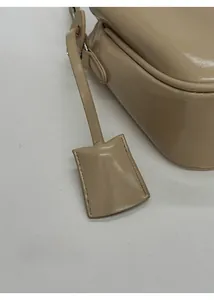 Detail der beige Ledertasche mit quadratischem Deko-Anhänger und sauberen Nähten am Riemen
