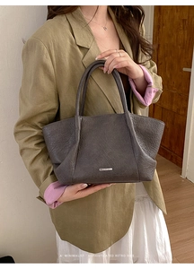 Détail d'un sac cabas en cuir anthracite avec logo métallique sur une tenue minimaliste