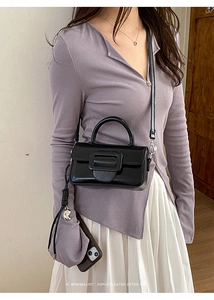 Dettaglio di una borsa in pelle lucida nera con una grande fibbia quadrata su una modella