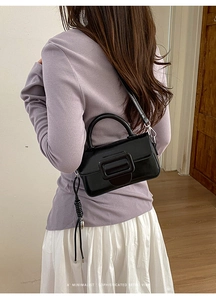 Borsa a mano nera lucida con fibbia indossata a tracolla su una modella di classe