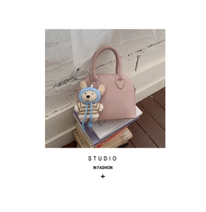 Detailed view of pink shell bag with lychee grain leather and bear charm on books