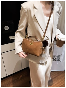 Detail einer braunen Kunstledertasche mit goldenem Reißverschluss und Plüschball-Anhänger