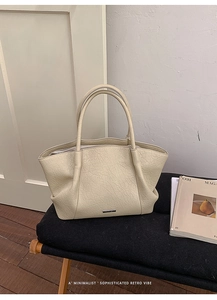 Détail d'un grand sac cabas crème en cuir texturé avec logo argenté sur velours noir