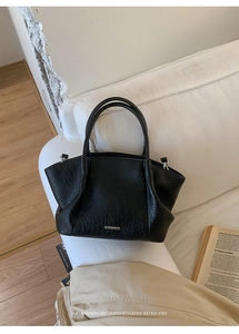 Détail de la texture d'un sac cabas noir en cuir avec logo en métal sur un canapé