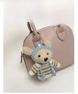 Detail of a handmade crochet bear charm with blue hat on a pink textured leather bag