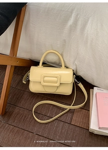 Dettaglio della borsa in pelle color crema con grande fibbia quadrata sul legno