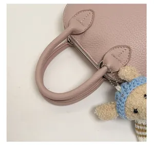 Detail of pink lychee leather handbag handle with cute bear pendant and silver hardware