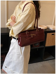 Close-up of a glossy burgundy patent leather shoulder bag with gold metal buckle detail