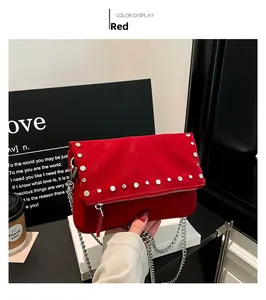 Détail du sac bandoulière en daim rouge avec rivets argentés et bandoulière chaîne à la main