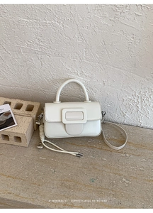 Dettaglio di una borsa minimalista in pelle PU color crema con fibbia quadrata e ciondolo