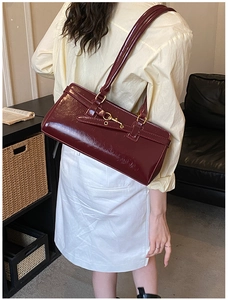 Detail of burgundy patent leather shoulder bag featuring vintage gold buckle and straps