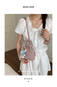 Detail of mauve shell-shaped crossbody bag with grain leather texture and bear charm