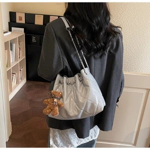 Close-up of light blue quilted bucket bag with metal chain and cute teddy bear charm
