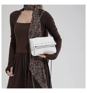 Close-up of a white leather crossbody bag featuring silver studs and a chain strap