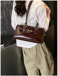Detail of dark chocolate glossy patent leather underarm bag with gold metal buckle