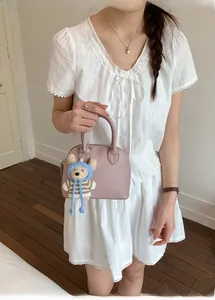 Detail of pink lychee leather shell bag with a cute knitted bear charm on white dress
