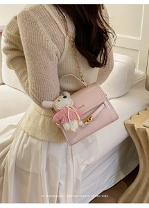 Pink bucket bag with gold chain strap and bear charm worn by a model in home setting