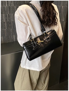 Detail of a black patent leather shoulder bag with gold buckle on a model in white shirt
