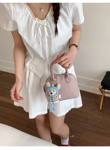 Pink shell handbag with lychee pattern leather and bear charm held by model
