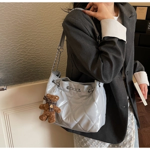 Detail of silver quilted underarm bag with metal chain strap and a cute bear charm