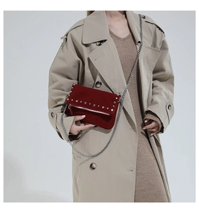 Detail of burgundy suede crossbody bag with silver rivets and metal chain strap