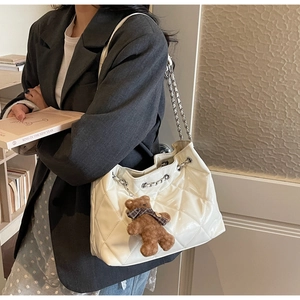 Detail of creamy white quilted tote bag with silver chain and cute brown bear charm