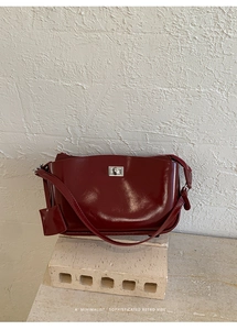 Detail der weinroten, glänzenden Leder-Baguette-Tasche mit silbernem Drehverschluss