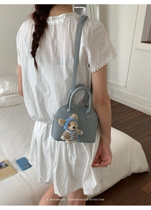 Detail of light blue shell bag in lychee texture leather with cute bear charm