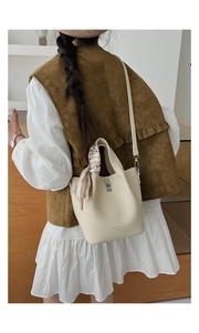 Detail of cream bucket bag with lychee texture, silk scarf handle and metal twist lock