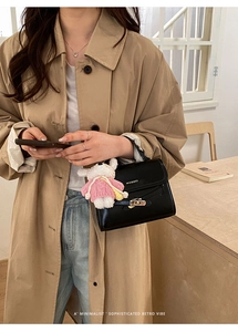 Detail of black leather bucket bag with gold clasp and plush bunny charm on khaki trench