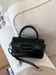 Borsa a mano in ecopelle nera lucida con ciondolo in argento su sfondo beige chiaro