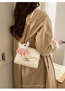 Close-up of a cream leather crossbody bag with a plush bear charm and gold chain