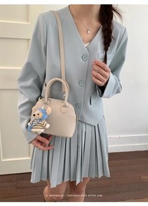 Chic beige shell bag with a cute teddy bear pendant worn with a light blue blazer