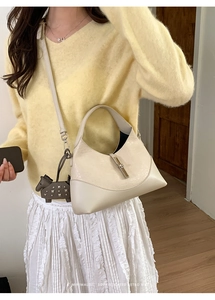 Minimalist beige moon bag with a decorative grey horse charm and metallic buckle closure