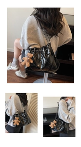 Close-up of black quilted bucket bag with gold chain strap and teddy bear charm accessory