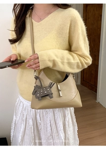 Detail of khaki leather bucket bag with a studded horse charm on a yellow sweater