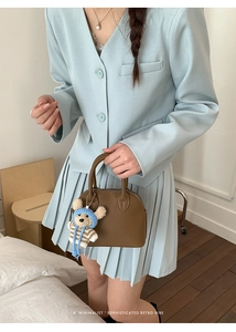 Close-up of a brown leather shell bag with a cute bear charm on a minimalist blue outfit