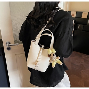 Detail of cream lychee leather bucket bag with metal lock and cute puppy pendant