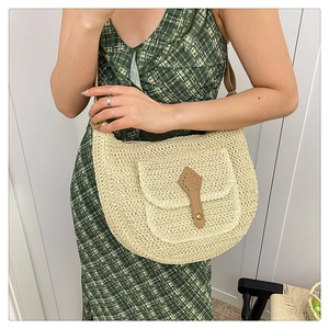 Détail du sac selle tissé avec lanière en cuir brun porté avec une robe à carreaux