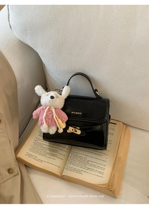 Detail of black mini bucket bag with gold lock and cute plush bear on vintage books