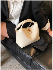 Detail of creamy white lychee grain leather bucket bag with gold twist lock and logo