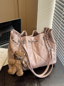 Chic pink quilted tote bag with silver chain straps and a plush bear charm on a desk