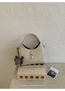 Close-up of contrast-stitched bucket bag with horse charm on stone pedestal